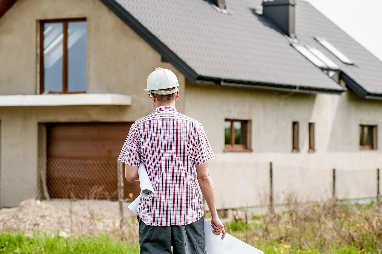 Geodeta w kasku i z mapą projektową idzie przy budynku, przygotowując podziały działek i wytyczenia